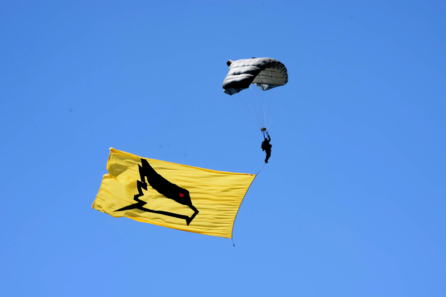 Paracaidista descendiendo con la bandera de la V Brigada Aérea en su tobillo