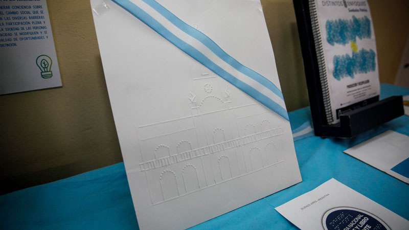 Dibujo del Calbildo hecho en braille con una cinta con los colores de Argentina atravezándola. 