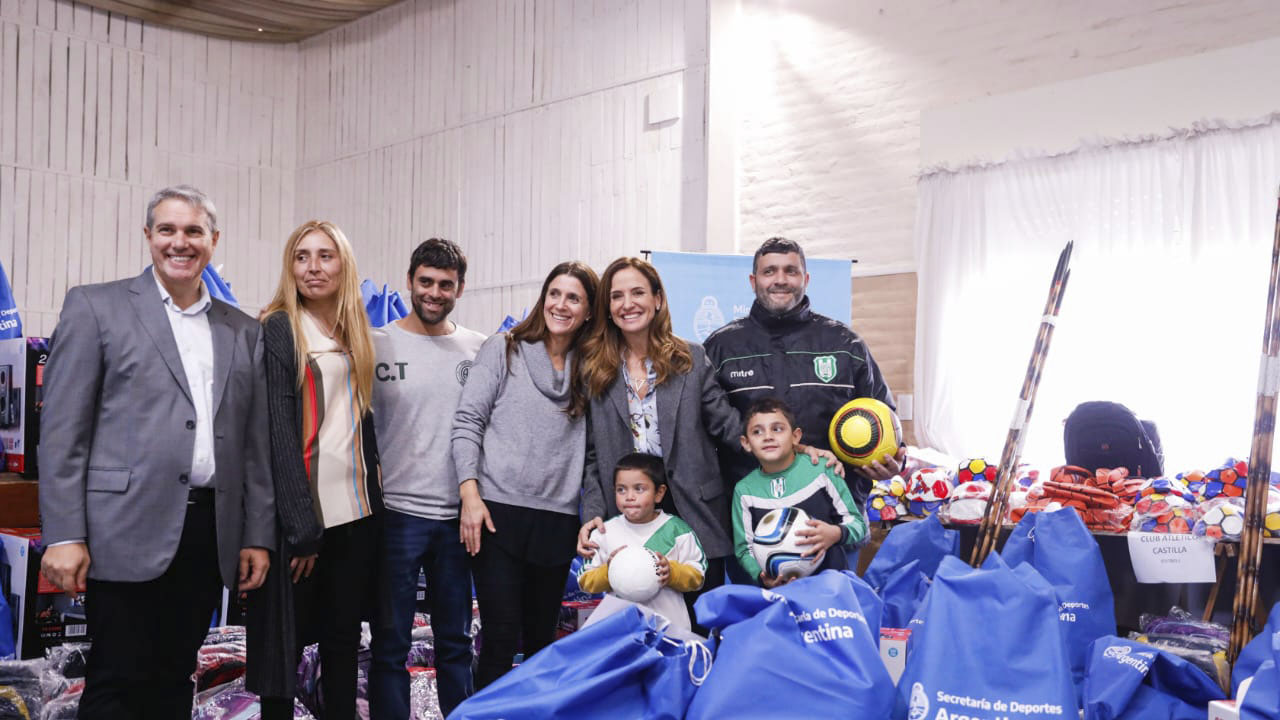 La ministra Tolosa Paz junto a funcionarios y varios niños que sostienen pelotas y materiales deportivos dentro del Club de barrio.