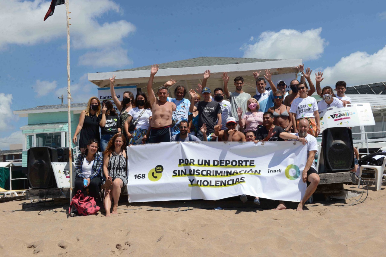 Personas sostienen una bandera en la playa con la leyenda "Por un deporte sin discriminación y violencias"