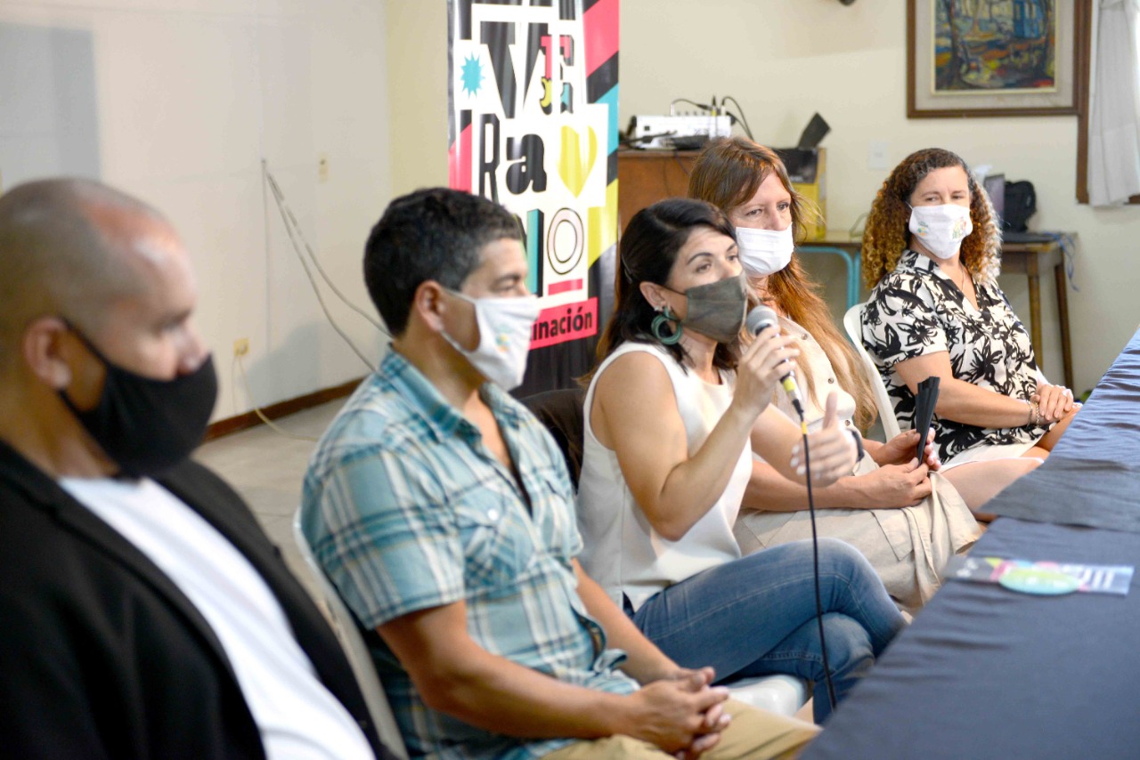 Lorena González hablando sentada en una mesa junta a funcionarios locales y del INADI