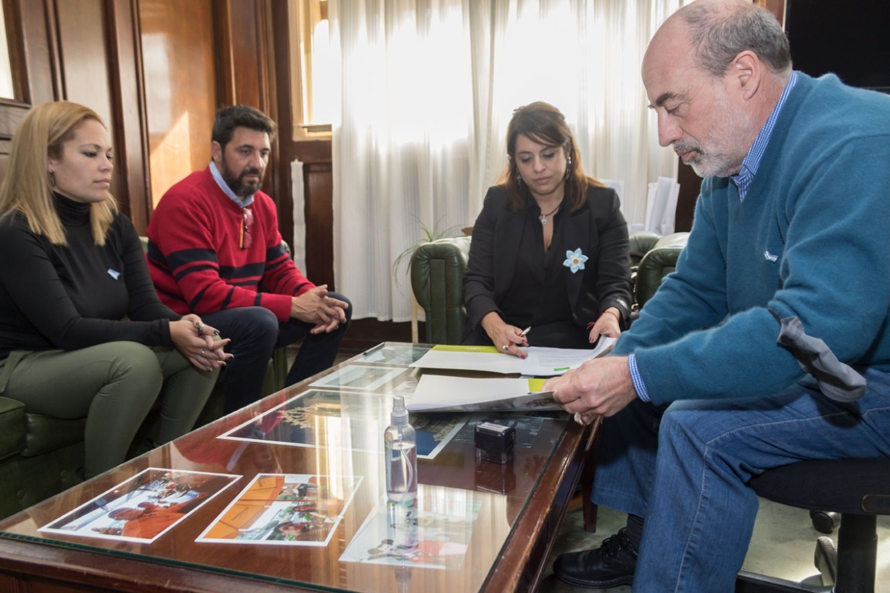 La titular del INADI junto al intendente y dos funcionarios más sentados firmando los convenios