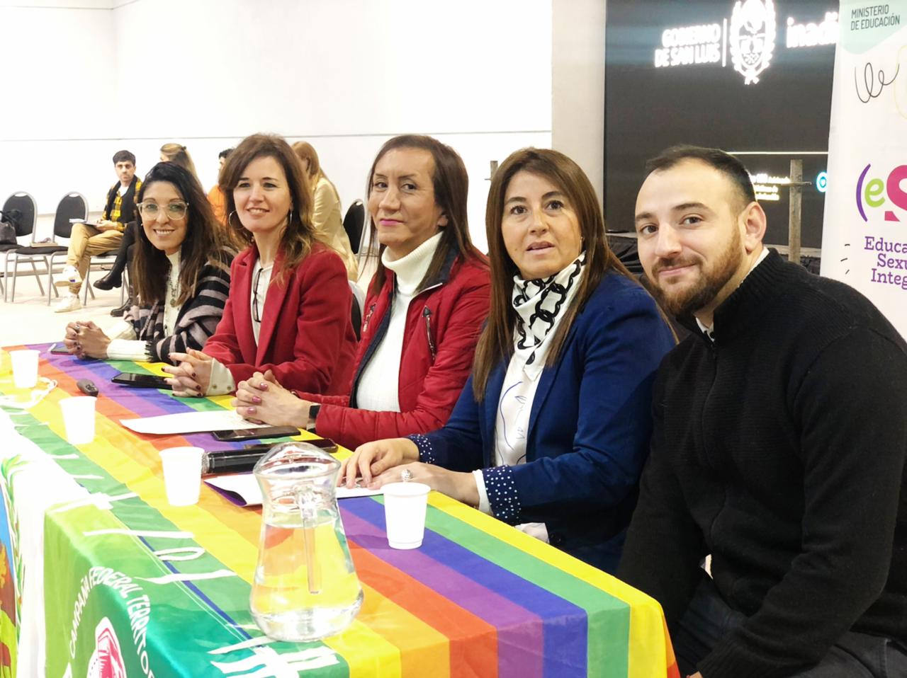 Funcionarios del INADI y locales sentados en la mesa panel con una bandera del orgullo posan a camara