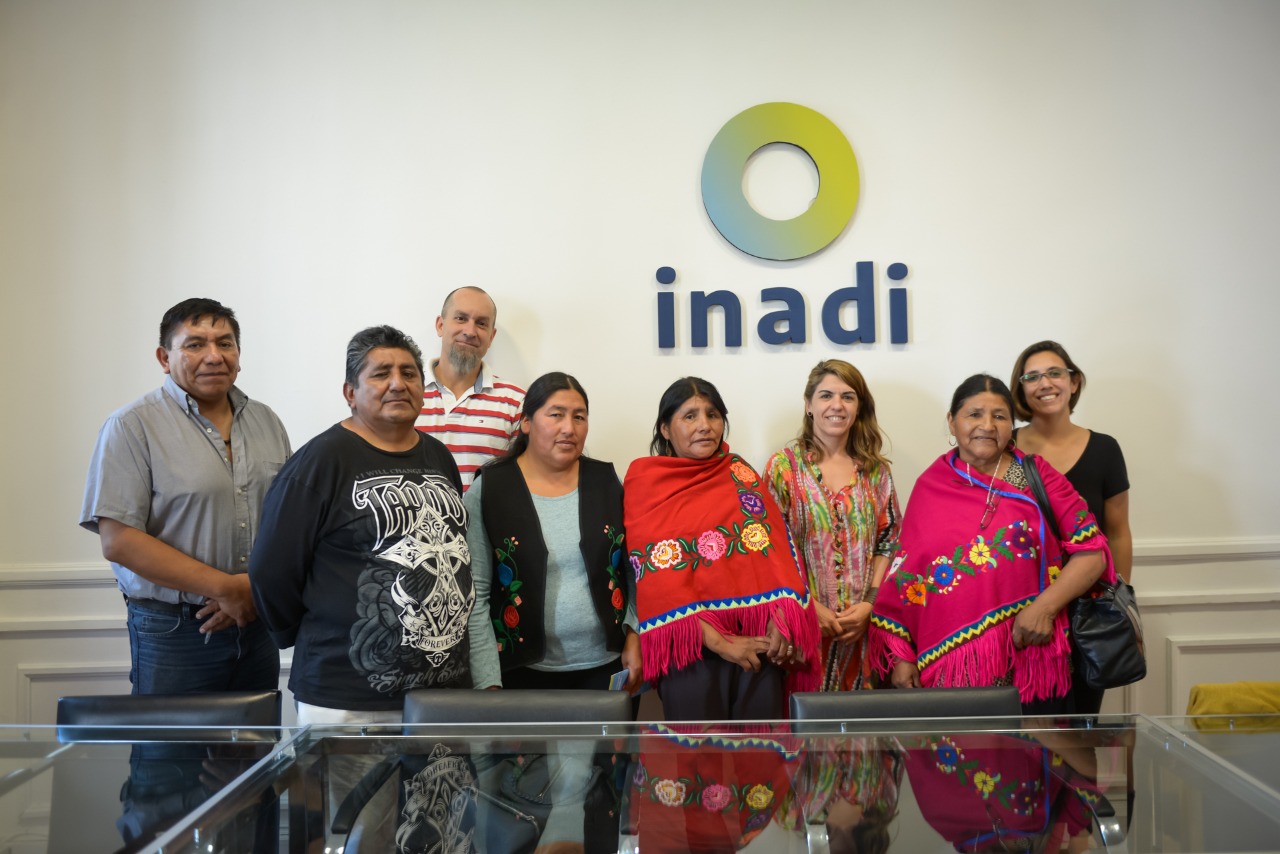 Todes les participantes de la reunión posan en la sala de reuniones con el logo INADI.
