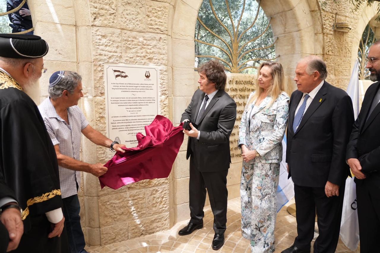 Karina Milei y el canciller Gerardo Werthein observan al presidente de la Nación descubrir la placa.