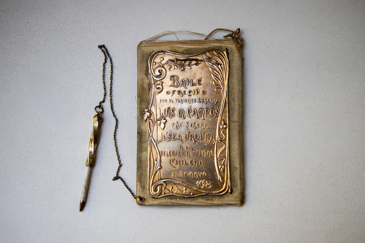 Libreta de baile. Obsequio de Luis María Campos y Justa de Urquiza y Costa Libreta de baile. Está hecha en seda y plata. En la tapa metálica tiene un texto. Tiene un lápiz que se encuentra atado a la libreta por medio de una cadena.