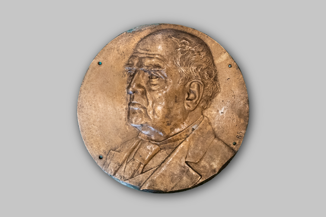 Fotografía color de una placa de forma circular que lleva la efigie del expresidente Domingo F. Sarmiento. La misma está hecha en altorrelieve de bronce.