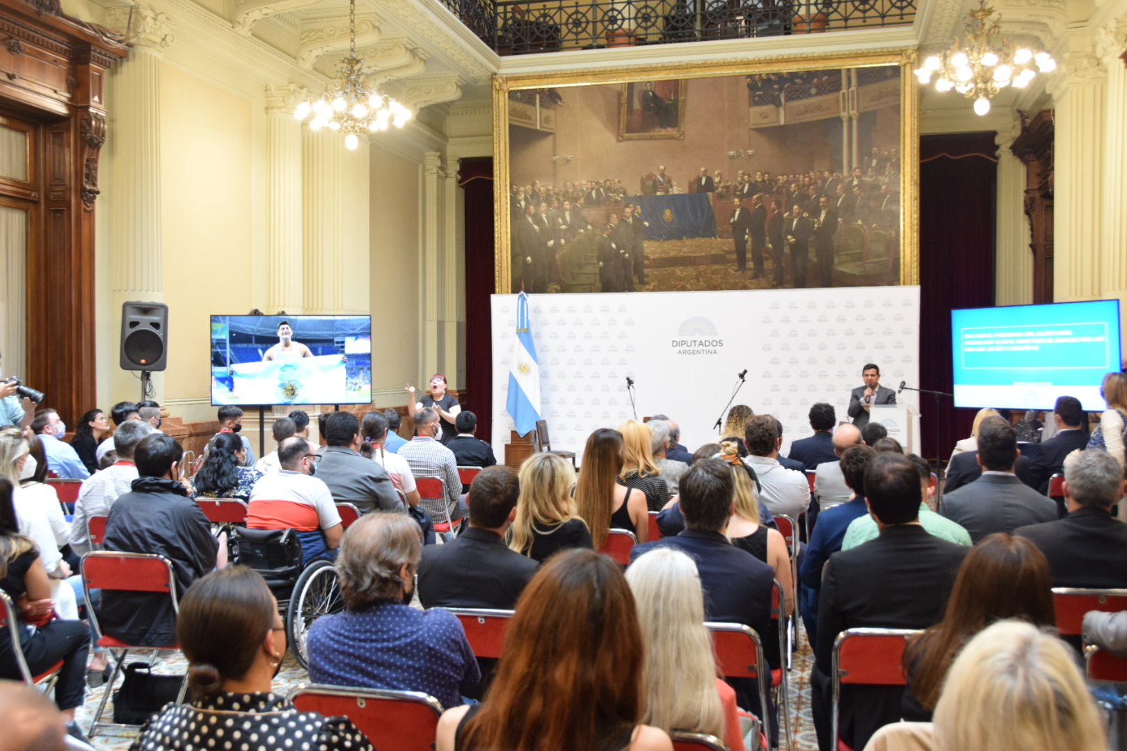 Imagen de Fernando Galarraga hablando en el atril del salón de los pasos perdidos del Congreso de la Nación Argentina junto a los deportistas paralímpicos y autoridades