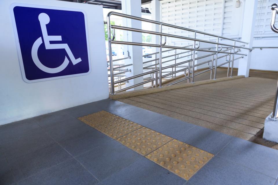 Fotografía de una rampa con señales podotáctiles y el símbolo de discapacidad.