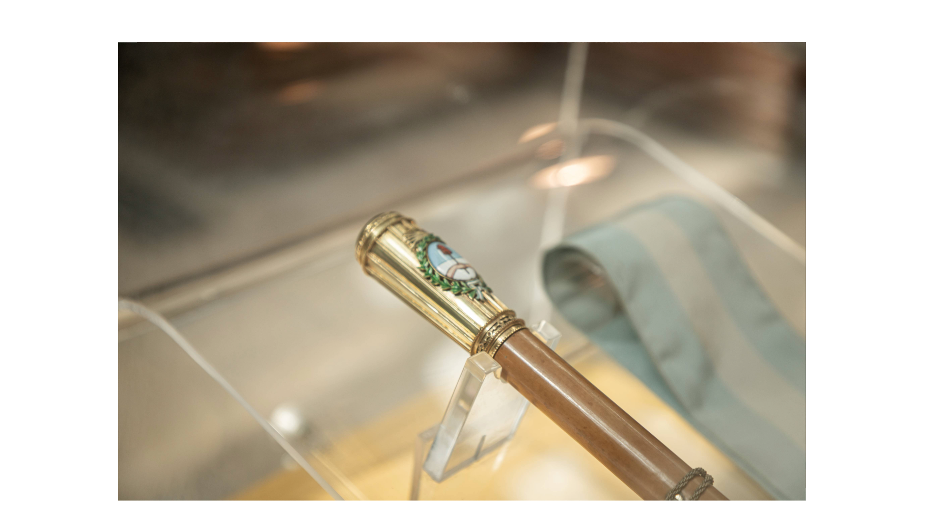 Vista del interior de una vitrina. La misma contiene la banda y el bastón de José M. Guido. La imagen muestra un detalle del bastón y de la banda.