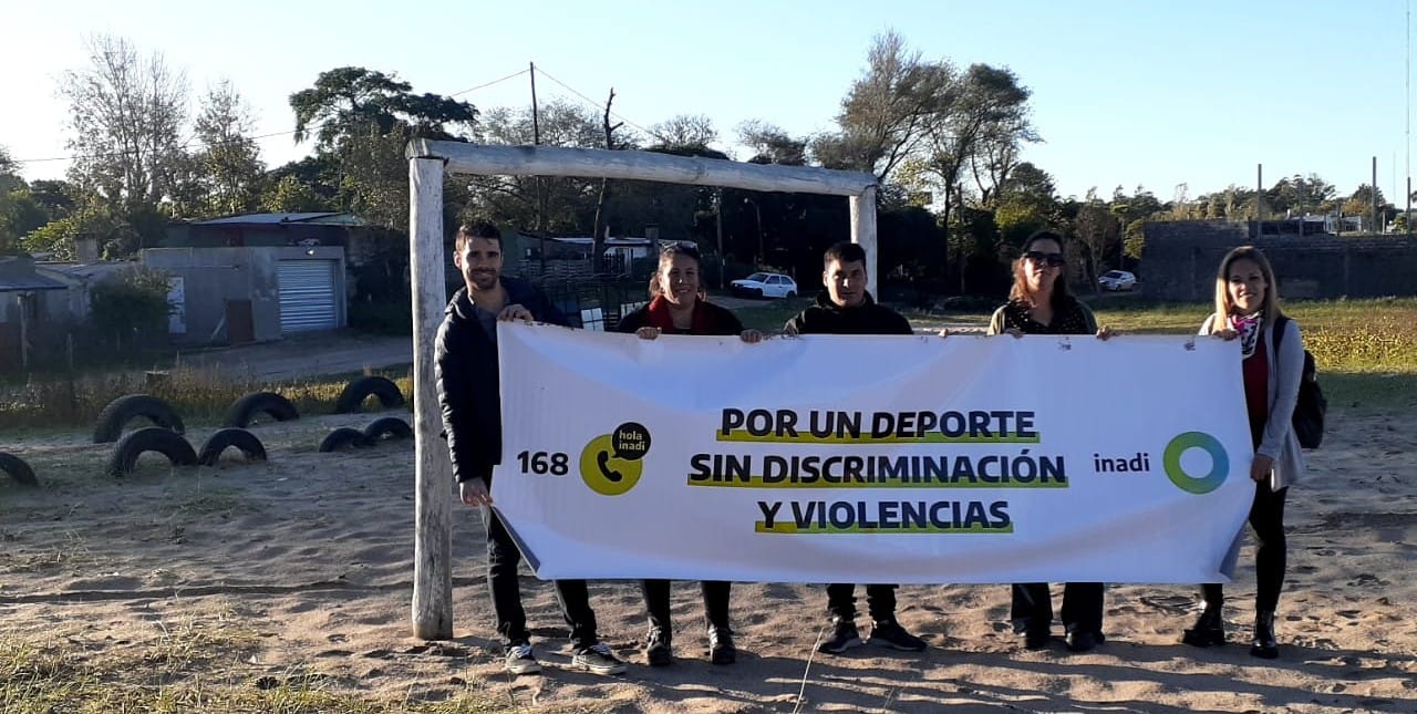 Los integrantes del INADI y los clubes posan con una bandera con el lema: "Por un deporte sin discriminación y violencias".
