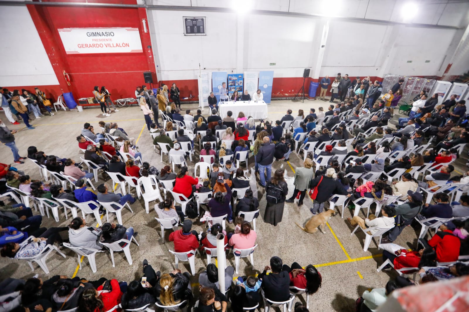 Panorámica desde arriba donde se observa la conferencia que brindó la ministra de Desarrollo Social, Victoria Tolosa Paz, junto a Andrés Larroque mientras las y los participantes escuchaban activamente del encuentro en el gimnasio del club Alumni.