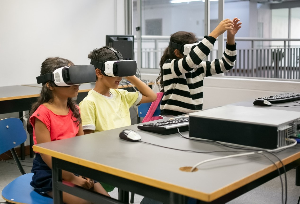 Fotografía de una niño y una niña sentados delante de una computadora con anteojos 4D