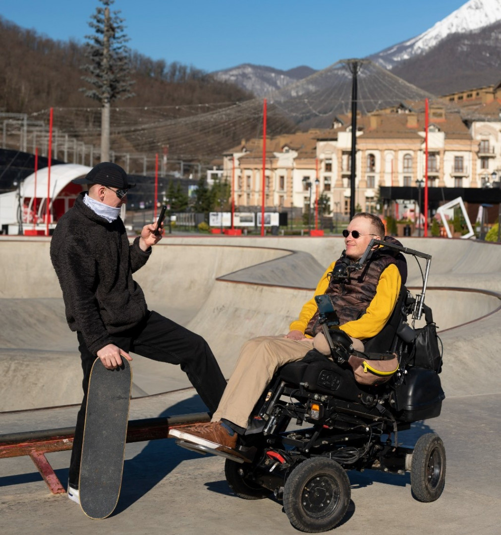 Fotografía de dos hombres, uno de ellos en silla de ruedas, en una zona urbana. 